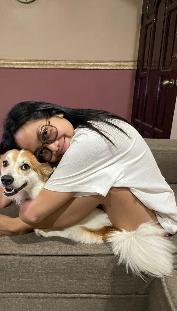 A person in a white shirt lovingly embraces a dog while sitting on a couch in a cozy living room setting.